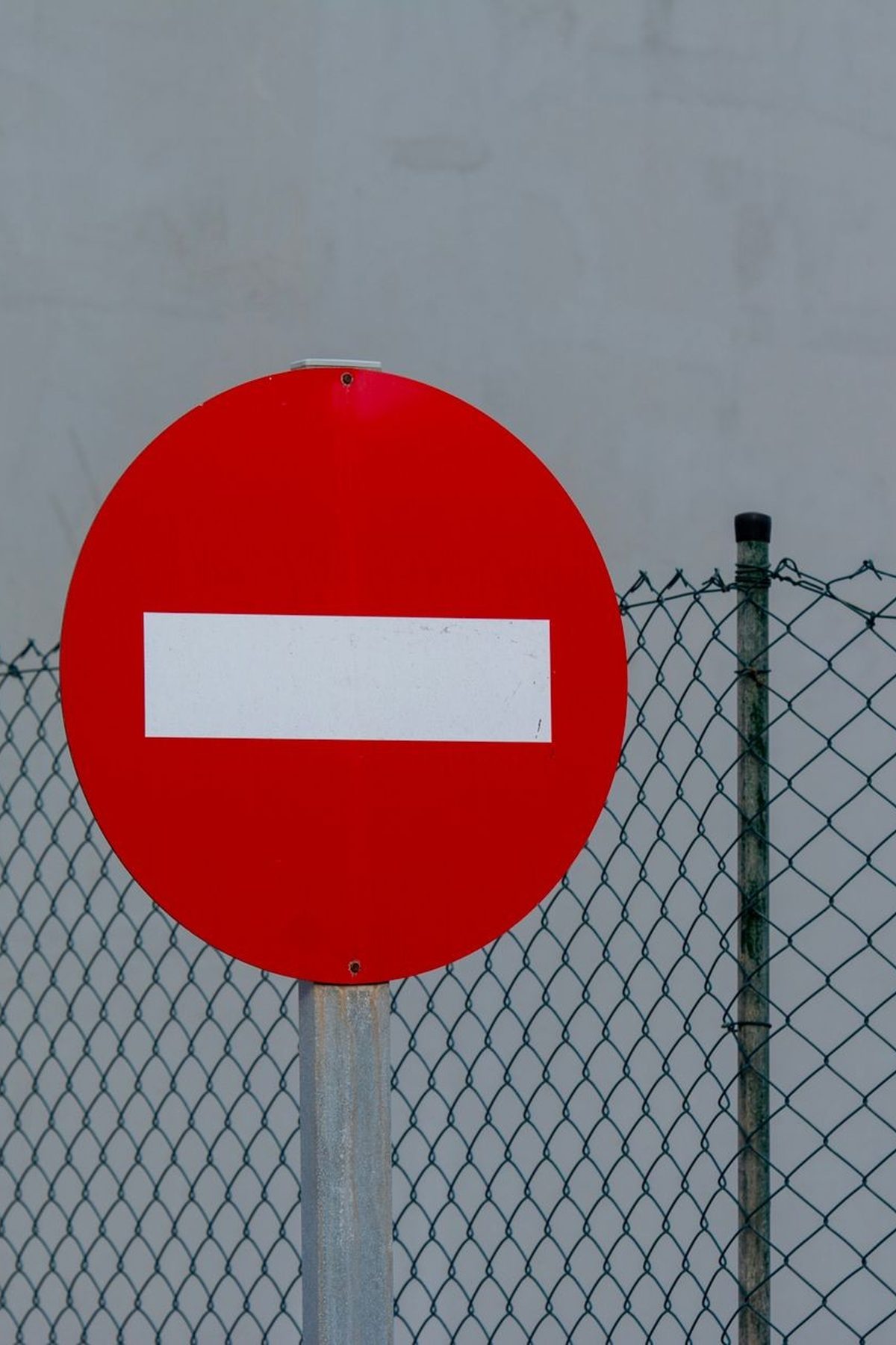 Red circular no entry sign in front of a mesh fence, symbolizing prohibition and security.