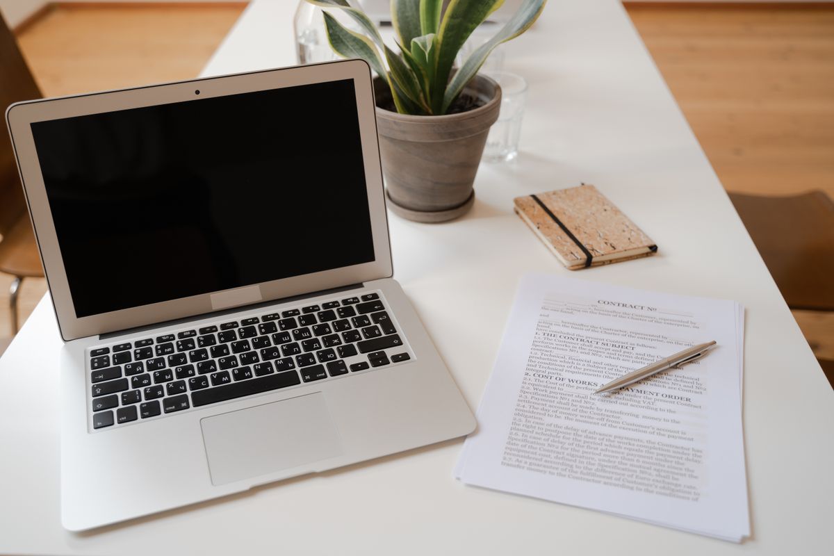 Otwarty laptop, doniczka z rośliną i dokument umowy na biurku