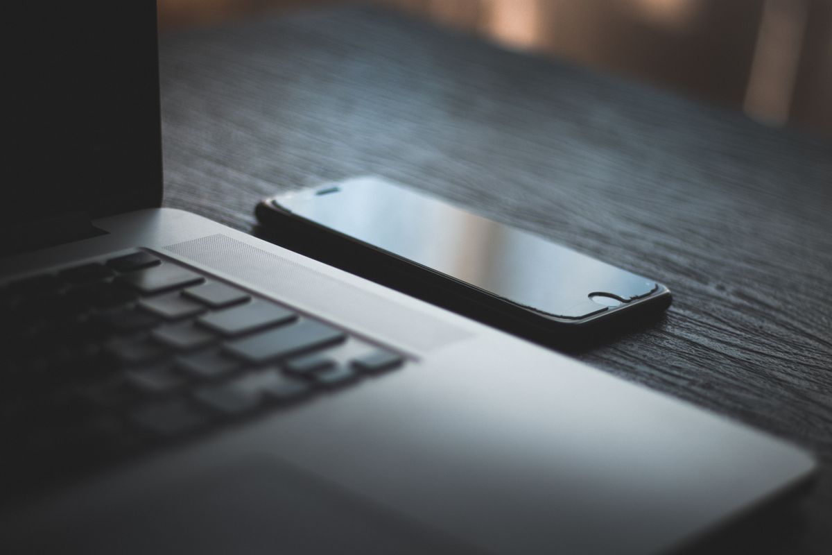 Smartfon leżący obok otwartego laptopa na drewnianym blacie