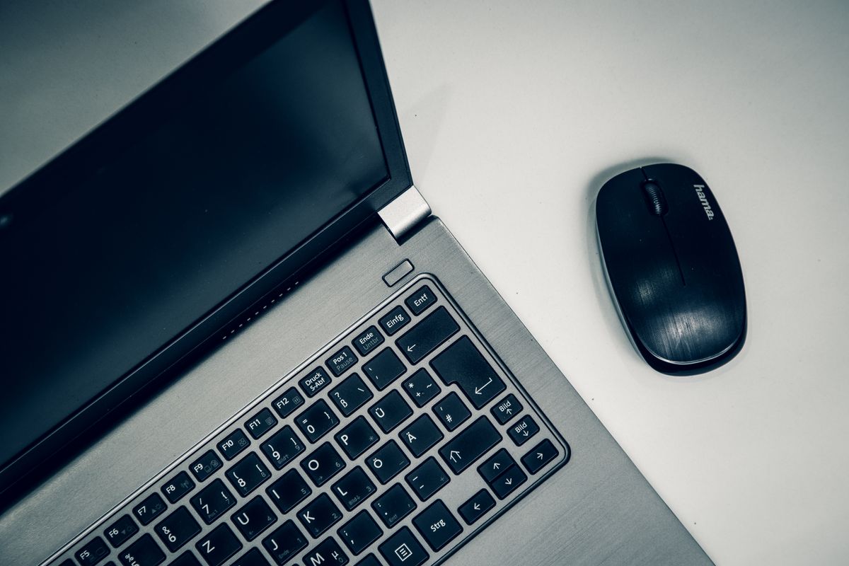 Srebrny biznesowy laptop z czarną klawiaturą obok myszki