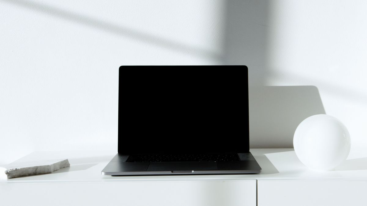 Czarny, otwarty laptop na białym blacie w jasnym pomieszczeniu