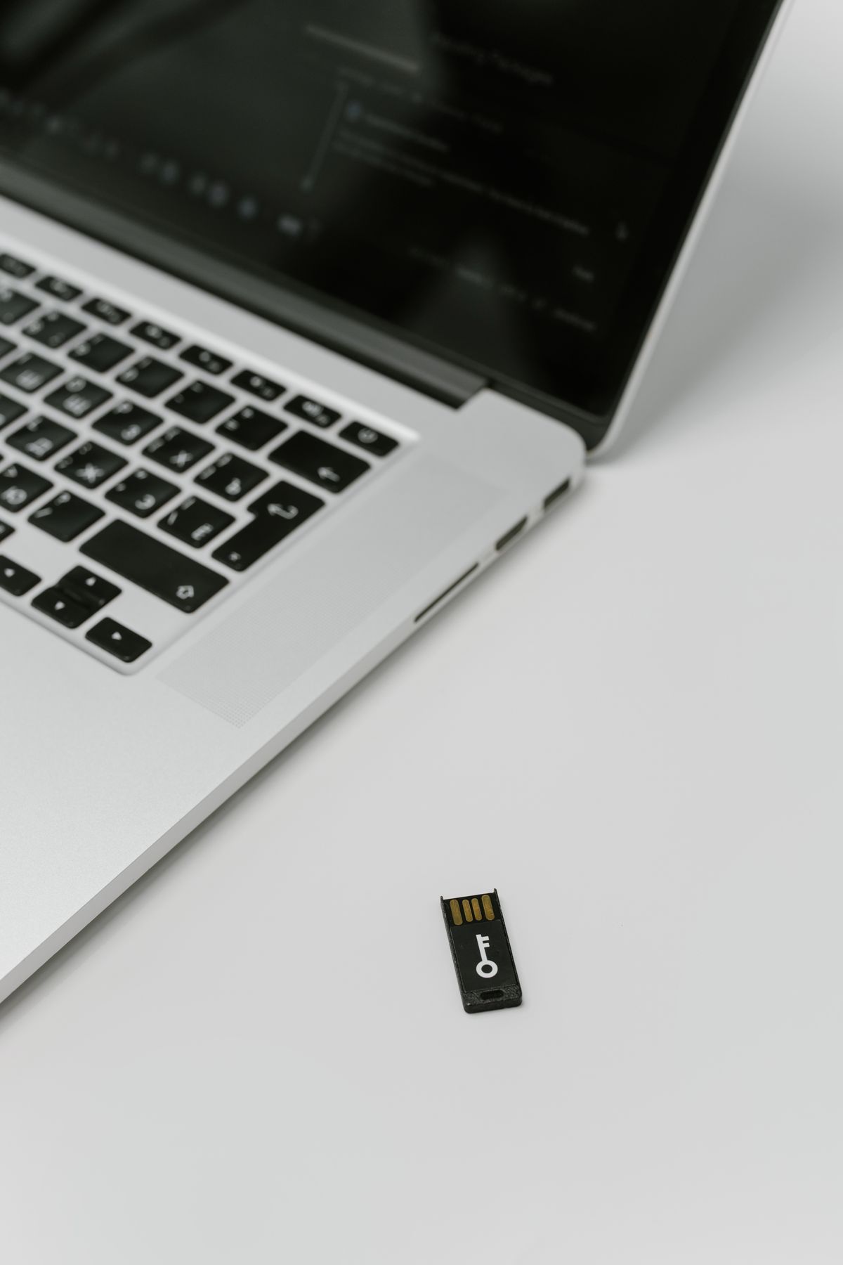 Srebrny laptop z czarnym kluczem zabezpieczającym USB leżącym obok