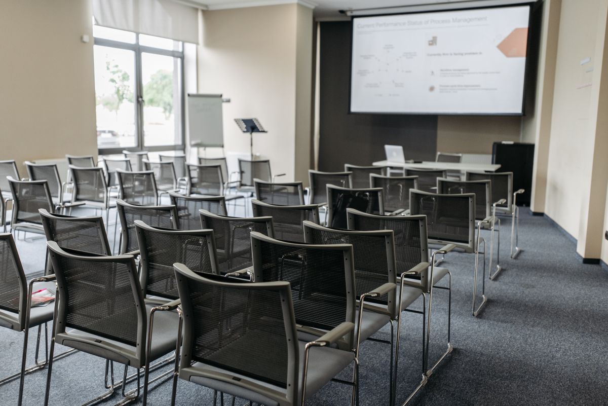 Pusta sala konferencyjna z ekranem projekcyjnym i laptopem na stole prelegenta