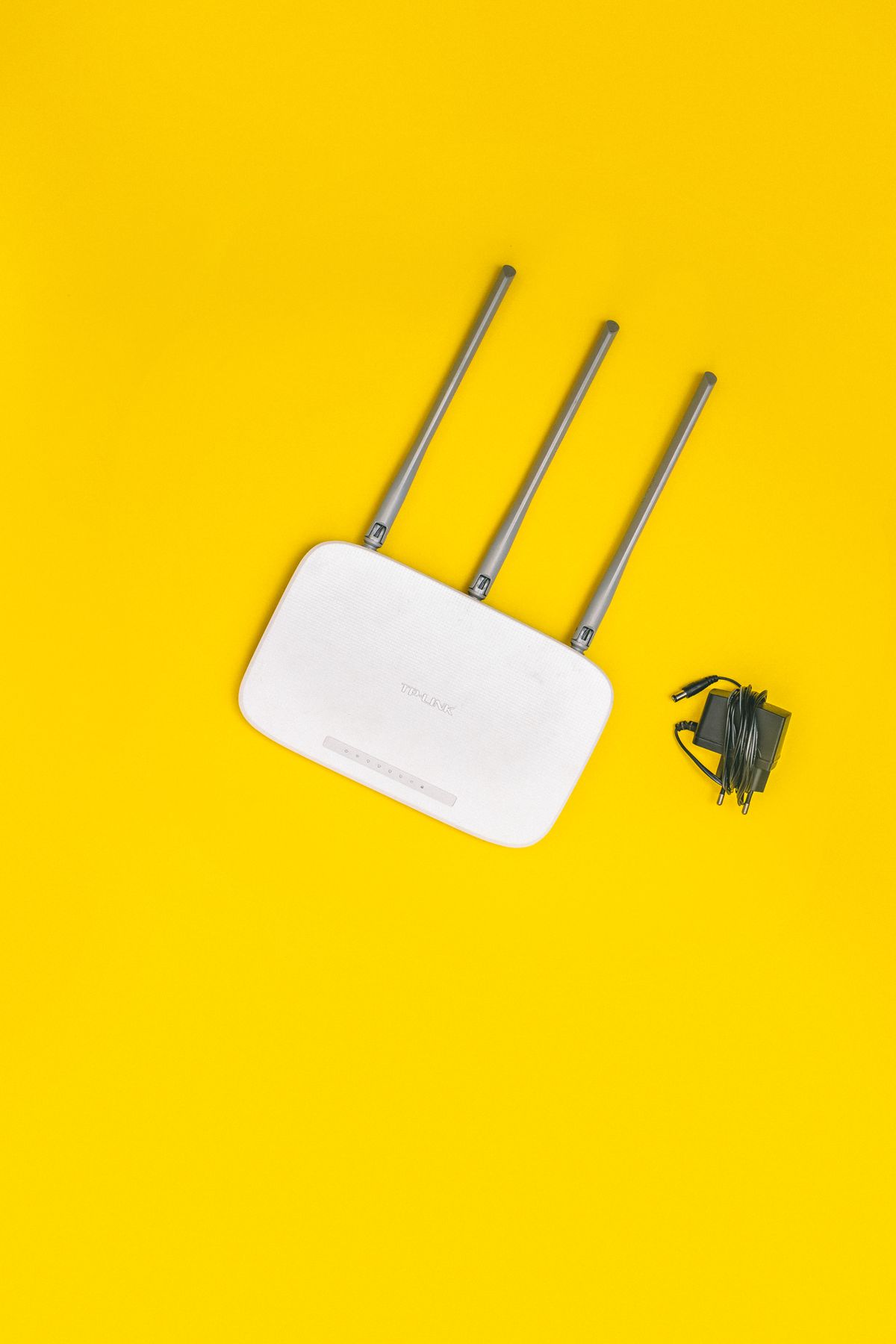 Biały router WiFi z trzema antenami i zasilaczem na żółtym tle