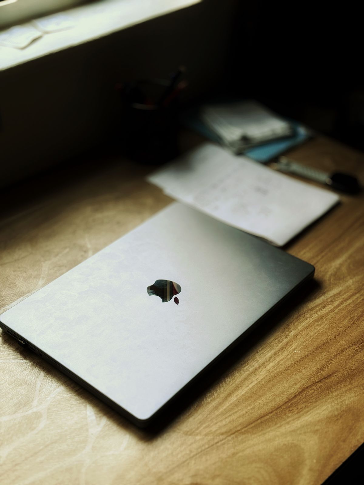 Zamknięty laptop leżący na drewnianym biurku obok kartek papieru
