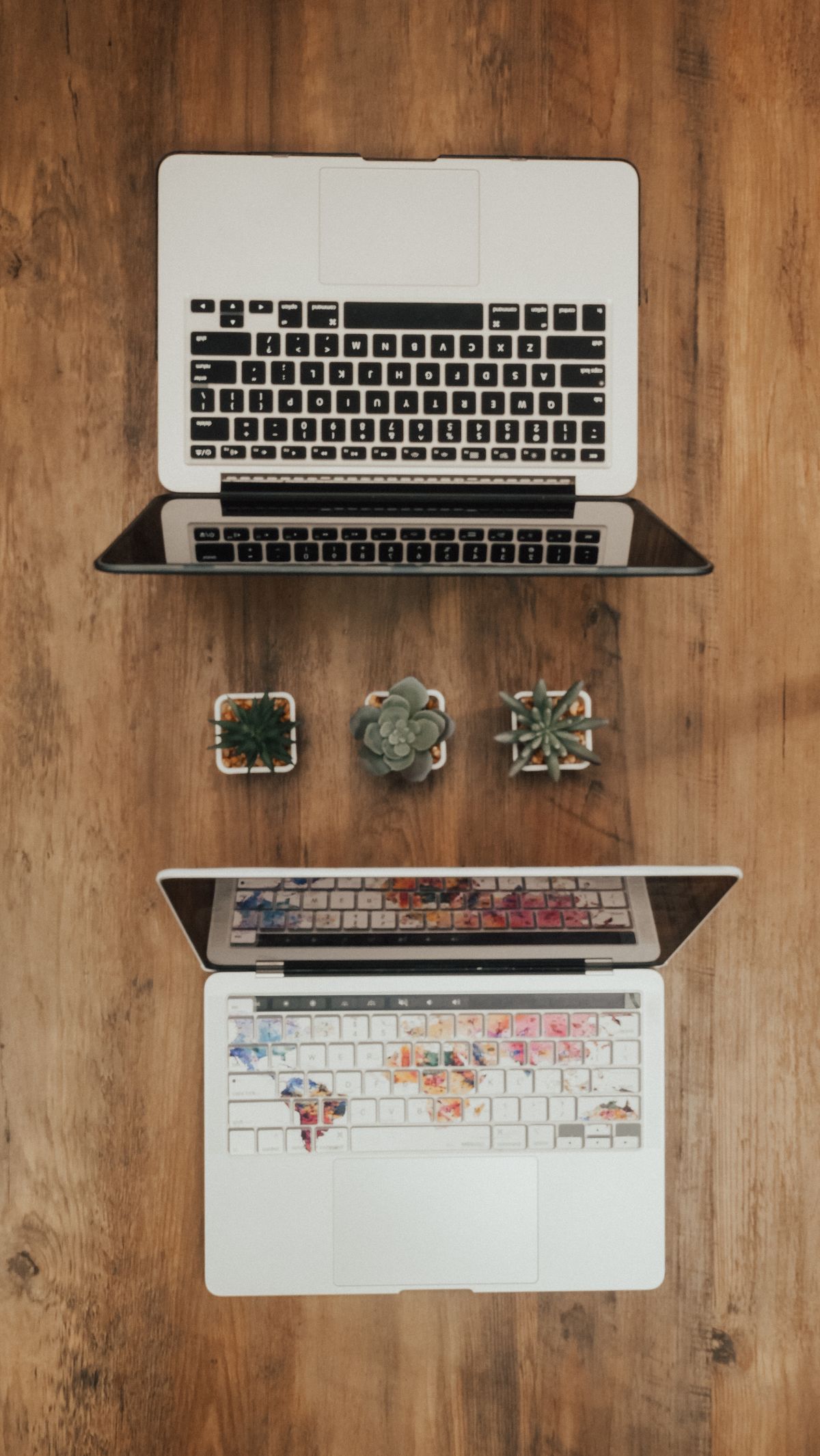 Dwa laptopy ułożone jeden nad drugim na drewnianym blacie