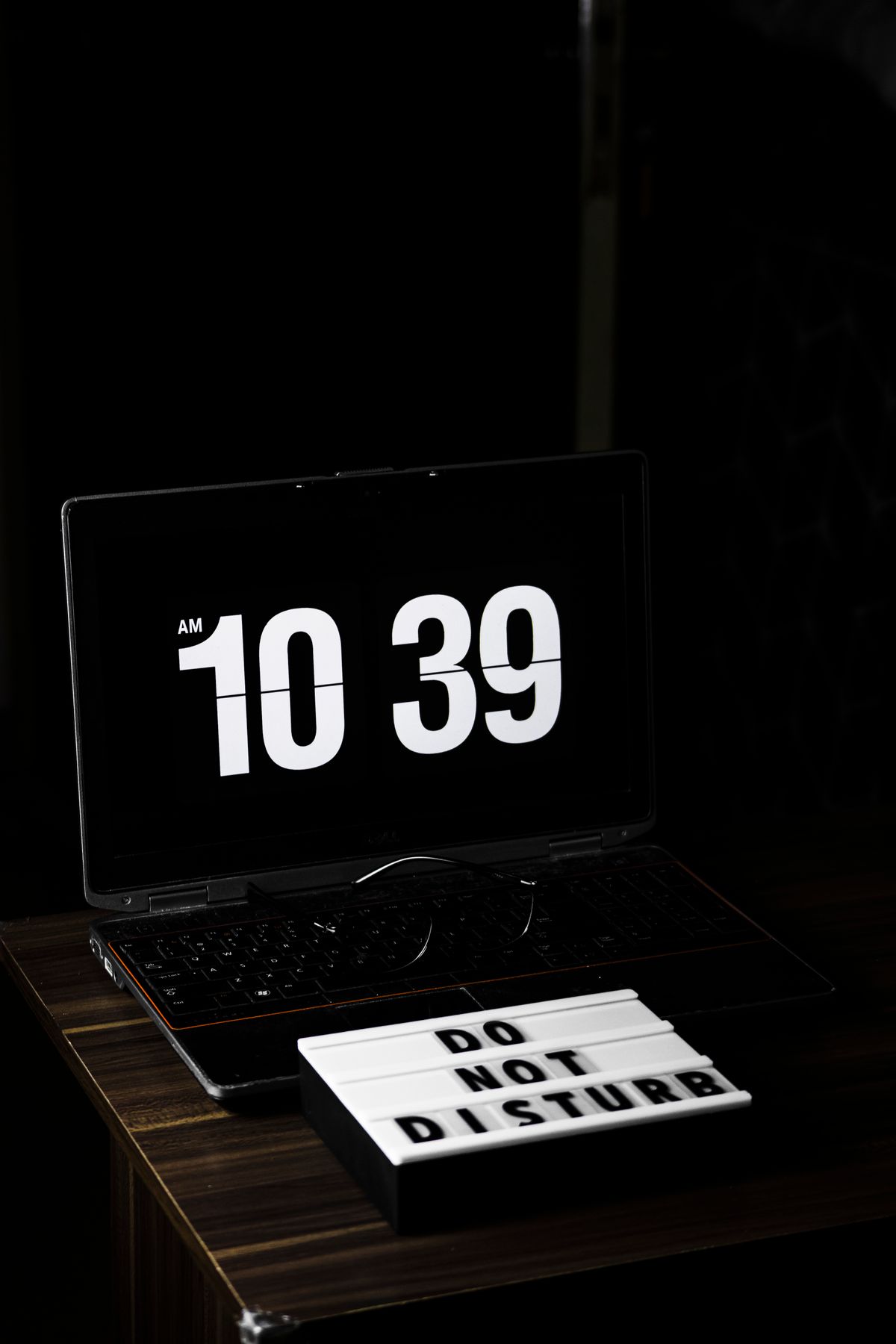 Laptop w ciemnym pomieszczeniu wyświetlający godzinę, obok tabliczka Do Not Disturb