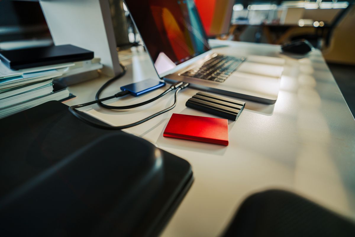 Zewnętrzne dyski przenośne podłączone kablami do otwartego laptopa na biurku