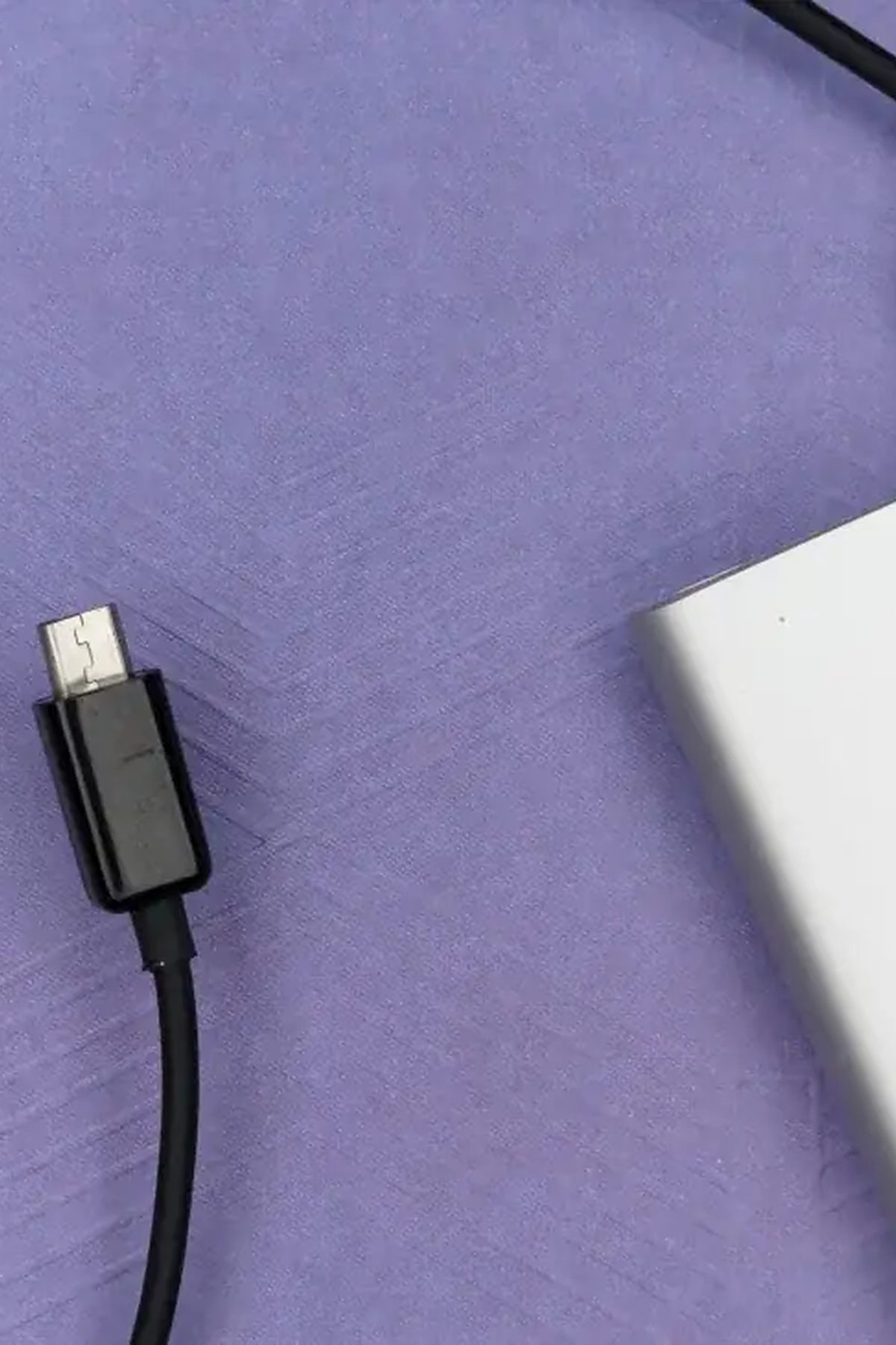 Kabel USB-C podłączony do przenośnego dysku SSD na fioletowym tle
